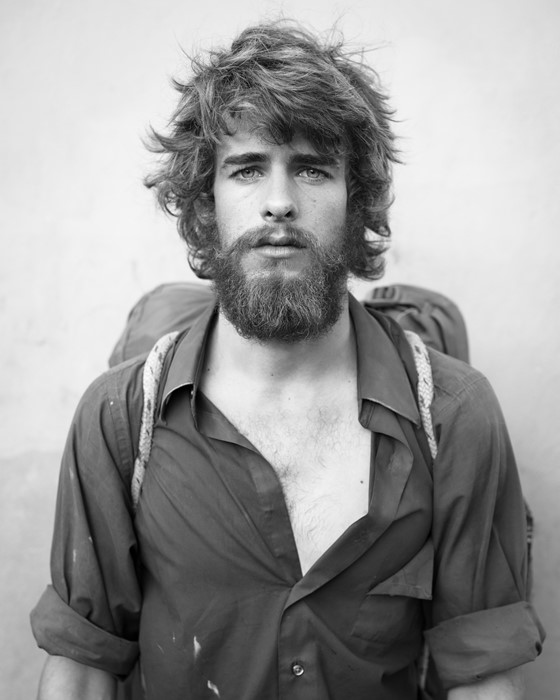 Portrait of a bohemian looking man with a rucksack, open shirt, and long hair and beard.