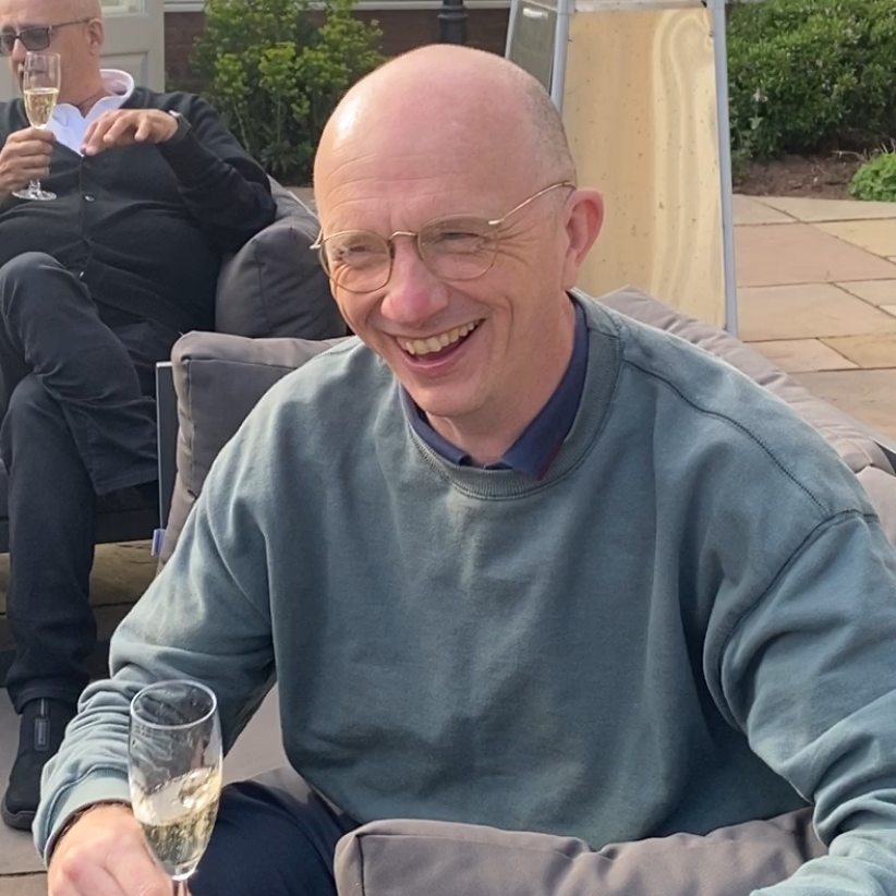 Phil Clark laughing while drinking a glass of wine outdoors.